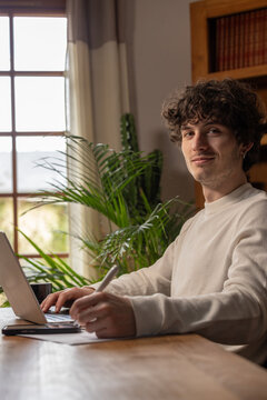 Jeune homme en t&eacute;l&eacute;travail utilisant un ordinateur portable dans un int&eacute;rieur lumineux et calme, incarnant la productivit&eacute; et le mode de vie professionnel moderne &agrave; domicile.