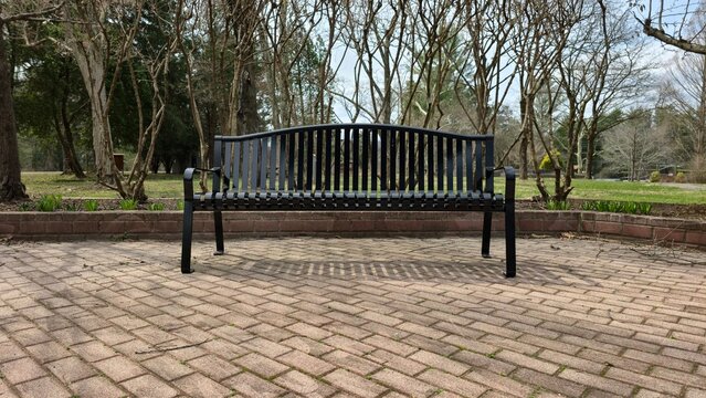 black metal park bench outdoor public seating in urban green space empty municipal infrastructure street furniture for city planning landscape architecture calm environment daytime static shot 1