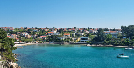 Fototapeta premium A wide scenic view showing the blue sea bay of Krk town with houses and lush green pine trees under a clear sky.