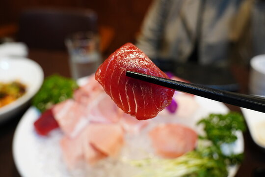 close-up photo of a piece of fresh tuna sashimi picked up with chopsticks.