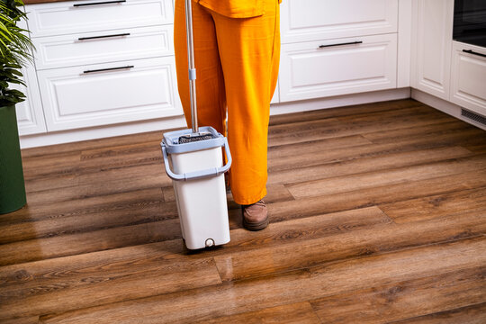 Woman cleaner standing with mop in bucket on wooden floor. Housekeeping service and domestic worker concept.