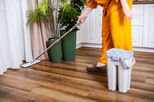 Woman housewife washing wooden floor with modern flat mop. Cleaning service process and household routine concept.