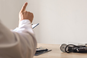 Closeup of male doctor consulting patient and gesturing with his hands. Medical expert giving advice, raising finger while holding clipboard