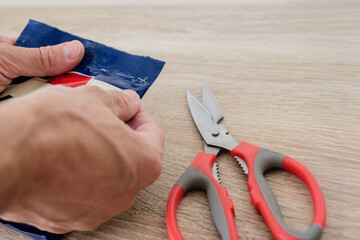 Male hands opening cocoa powder package with scissors. Opening food package by hand, close-up of fingers and sealed foil bag