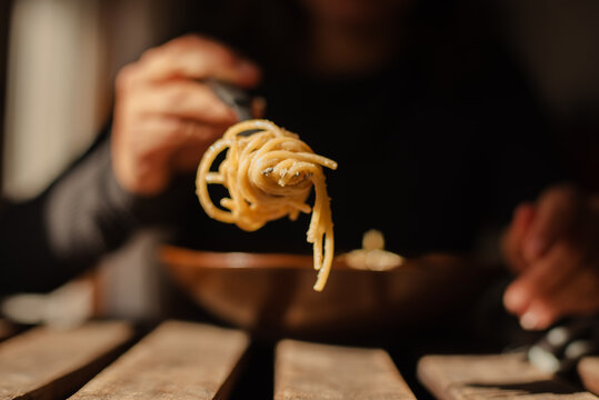 Unrecognizable person with spaghetti wrapped around a fork in the foreground.