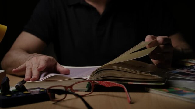 Person turning pages of open book with hands, reading and studying indoors in di