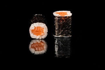 Two salmon maki sushi rolls with nori seaweed and white rice, one showing cross section with fresh salmon filling, isolated on black background with mirror reflection. Part of sushi roll series, studi © Vitaliy