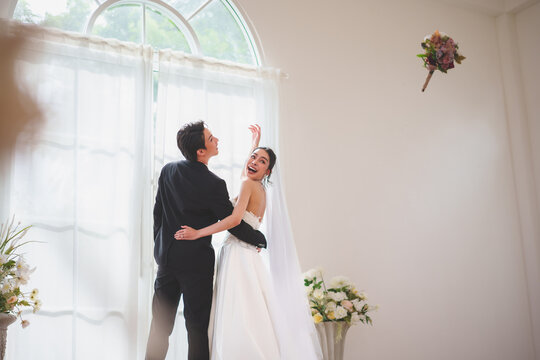 Asian bride throwing bouquet during wedding celebration indoors
