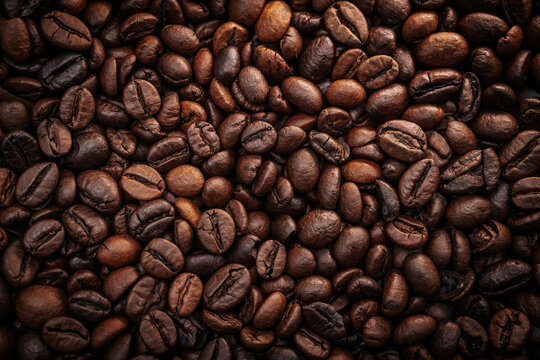 Close-up view of roasted coffee beans showcasing rich textures and varying shades of brown, arranged densely on a dark surface for a natural, organic appearance