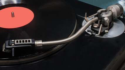 A vintage vinyl record player with a record mounted on it. The platter holding the record, the tonearm with the cartridge and stylus. © miraleks