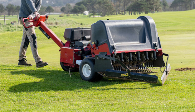 Groundskeeper aerating golf course green with professional turf maintenance machine on sunny day sports field care concept