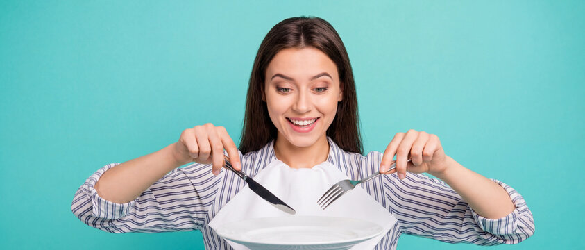 caucasian woman holding knife and fork looking excitedly at empty white plate over turquoise background with copyspace. diet, hunger, fasting concept. banner, website header.