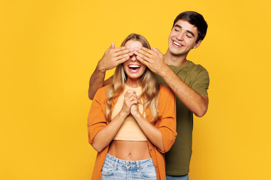 Young fun couple two friends family man woman wear shirt casual clothes cuddle embrace together close eyes with hands play guess who or hide and seek isolated on pastel plain yellow background studio.