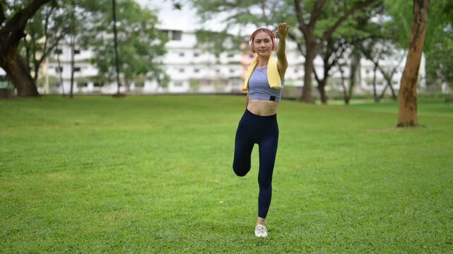 A woman is doing a yoga pose in a park. She is wearing a blue top and blue pants