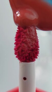 Placing or applying lip tint onto the brush tip slowly. Close up view, precise makeup application, cosmetic product detail on clean white background.