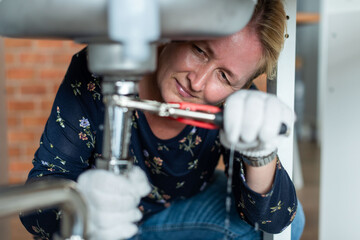 Woman fixing kitchen sink pipes
