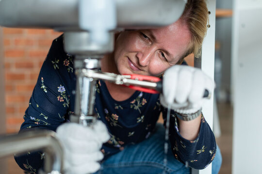Woman fixing kitchen sink pipes
