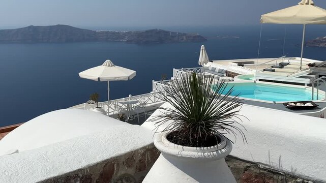 White architecture in Santorini island, Greece. Terrace with swimming pool and sunbeds. Blue sea and the blue sky at sunny day. Travel and summer vacation concept. 
