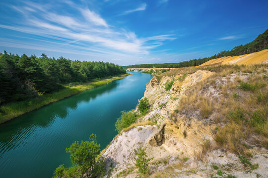A bright blue river flows through a deep canyon with sandy cliffs and green pine trees under a clear sky. Scenic river landscape, summer nature, outdoor adventure.