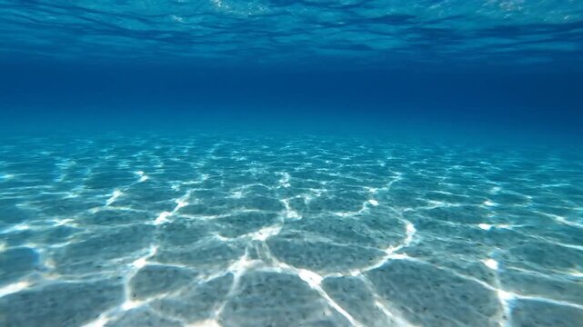 A tranquil underwater view showing sunlight caustics dancing on the white sandy floor of a clear blue ocean, creating a serene and shimmering environment.