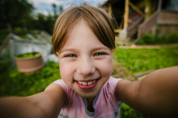 Fototapeta premium Happy young girl taking a wide angle selfie outdoors in a green garden with strong perspective distortion and blurred background.