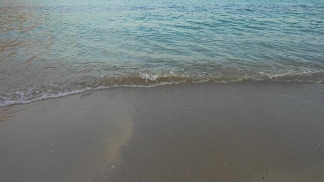 Sea waves washing over sandy beach with crystal water.
