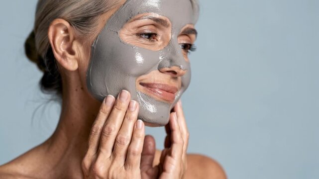 Mature woman enjoying relaxing facial mud mask skincare routine for healthy glowing skin