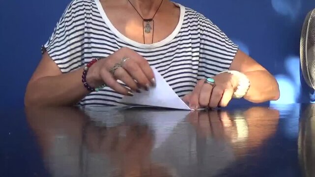 81. Young woman making a paper boat on the table. A woman folds a piece of paper and makes a boat out of it, showing it to the children