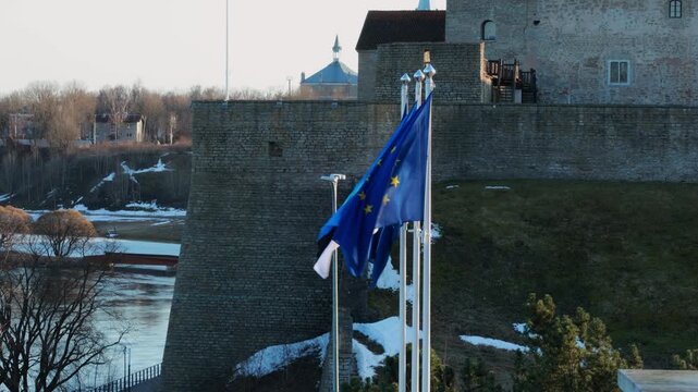 Narva, Estonia &ndash; April 2026 Estonian flag moving in the wind on a flagpole above natural landscape with river and trees in early spring season.