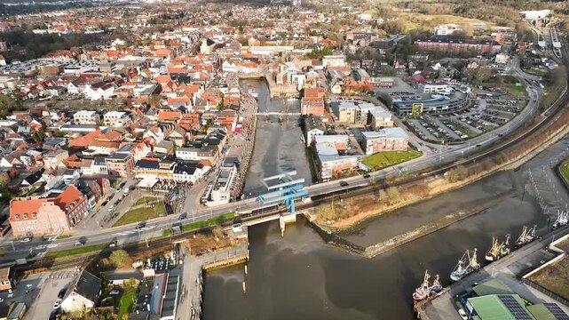 Aerial footage of Husum harbor with blue folding railway bridge, fishing boats docked in the canal and traditional North Frisian buildings of the old town, Germany.