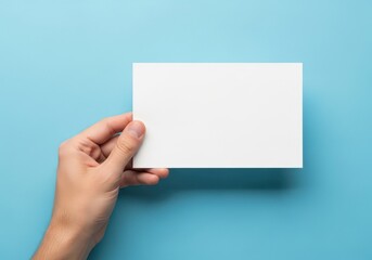 Obraz premium A hand holding a blank rectangular piece of white paper against a solid light blue background.
