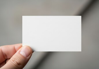 Fototapeta premium A person holding a blank white business card against a neutral gray background for design mockup