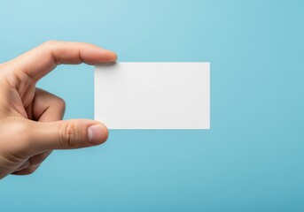 Obraz premium A hand holding a blank white business card against a solid light blue background for presentation