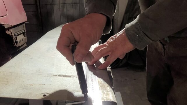 Hands are seen measuring and marking a metal sheet with precision tools in a dimly lit workshop. The person is focused on ensuring accuracy in their work as evening light filters in.