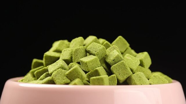 pile of dried cat grass cube rotating slowly in a pet bowl on a black background. close-up shot