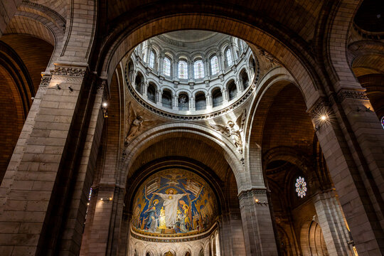 Interior view of the Basilica of the Sacred Heart of Montmartre showing the central dome with mosaics, the nave and colored stained glass windows in warm light, in Paris, France.
