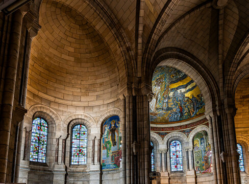 Interior view of the Basilica of the Sacred Heart of Montmartre showing the central dome with mosaics, the nave and colored stained glass windows in warm light, in Paris, France.