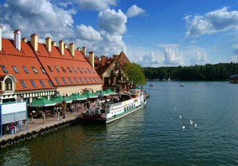 View of the Mikolajki harbor promenade with historical buildings and a cruise ship docked at the pier. Sunny day in the sailing capital of Poland. © puchan