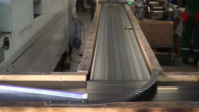A conveyor belt transports small caps throughout a busy warehouse. Workers closely monitor the system as objects move quickly along the rails.