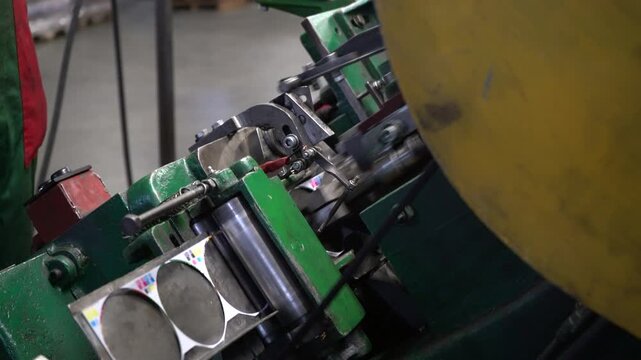 Workers are shaping metal parts on a machine in an industrial workshop. The process involves careful handling and precision adjustments throughout the task.