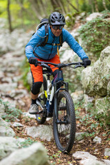 Fototapeta premium Experienced mountain biker riding a rocky forest trail wearing helmet, backpack and bright gear