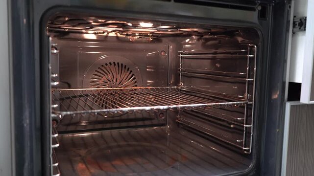 In an open oven there is a fan behind a metal grill.