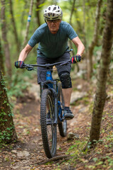 Naklejka premium Experienced man mountain biking on a narrow forest trail wearing helmet and knee pads