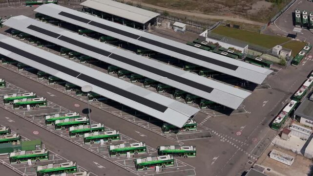 Aerial drone scene of an electric bus depot in Milan, Italy. Multiple buses lined up and charging create a structured visual of modern transport infrastructure and environmentally friendly urban mobil