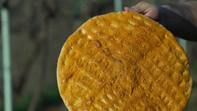 A cinematic, close-up shot of a traditional Albanian blessed bread, known locally as "buka e bekuar," slowly rotating. The video highlights the intricate, handcrafted patterns and symbolic decorations