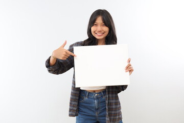 Fototapeta premium A smiling teenage girl looks at the camera while pointing at a blank white board she is holding, space for text, isolated gray background.