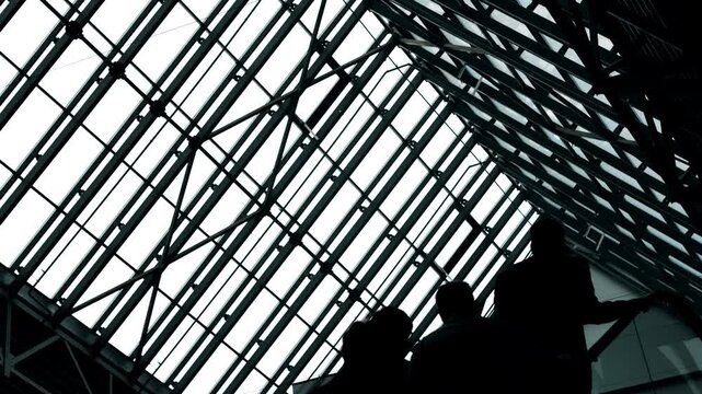 Silhouettes of business people moving on escalator inside modern glass building concept of corporate flow urban architecture and professional environment indoors.