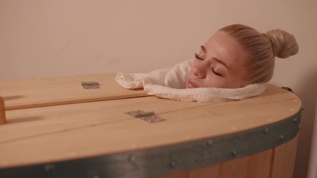Young woman relaxing in wooden sauna phyto barrel at spa, enjoying wellness treatment, detox and body care concept