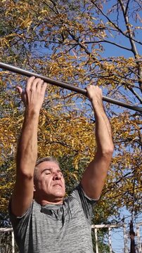 Fit Mature Man Performing Chin-ups at Outdoor Gym on Sunny Day. Video is ideal for promoting fitness and outdoor workouts. Series Track Code: Fit-Mature-Man-54-Outdoor-Fitness-Series-2024
