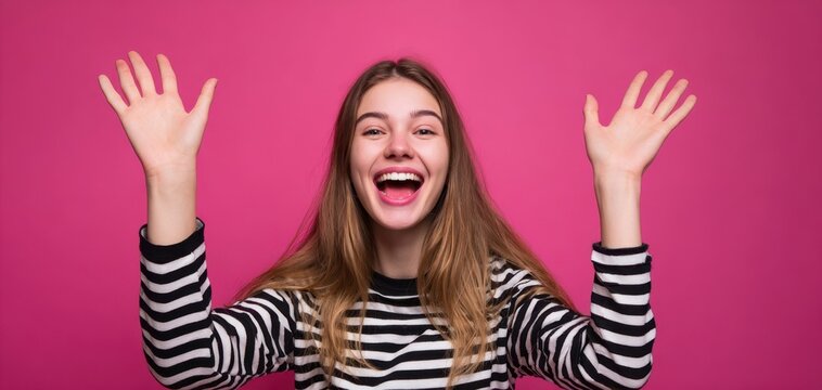 The young woman celebrating with raised hands against a bright pink background